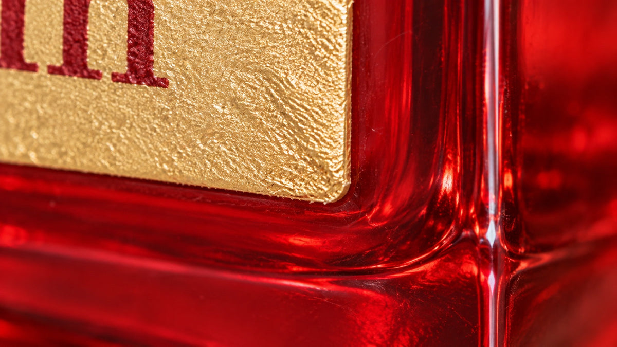 Ultramakroaufnahme der goldenen Etikettkante auf dem rubinroten Glas von Baccarat Rouge 540 Extrait.